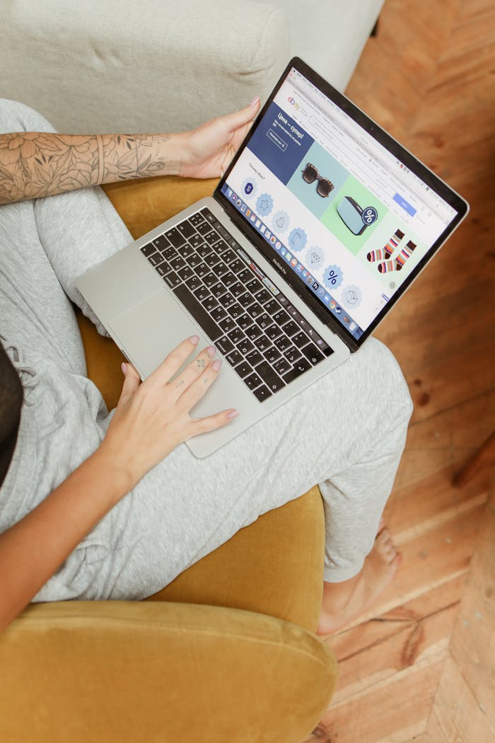 Woman using a laptop to browse online shopping, sitting comfortably in a cozy indoor setting.